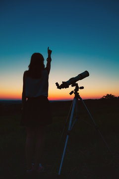 Girl looking at the stars with telescope beside her.
