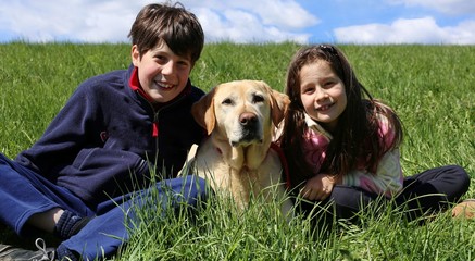 young brother and little sister smiling with their labrador dog