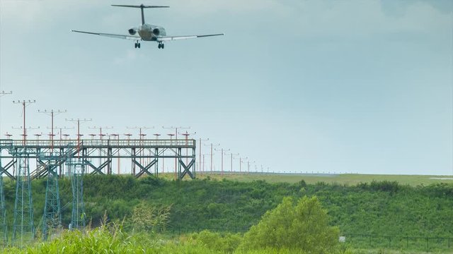Airport Final Approach Closeup at the Edge of a Runway with a Landing Commercial Passenger Airliner Flying Over Directional Safety Lights with Green Summer Foliage and Grass
