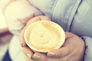 Young woman is drinking coffee on the street while walking on cold winter day. Hands with white take take-out coffee paper cup. Coloring and processing photo with soft focus in instagram style.