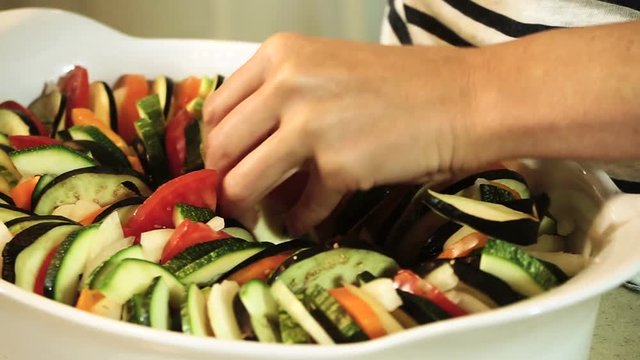 Cooking ratatouille. Female hands laying out the chopped vegetables in a baking dish. HD