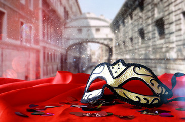venetian mask on red silk fabric in front of blurry Venice