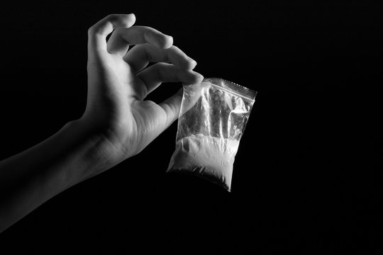 Packet With White Narcotic In Hand On Black Background, Monochrome Image