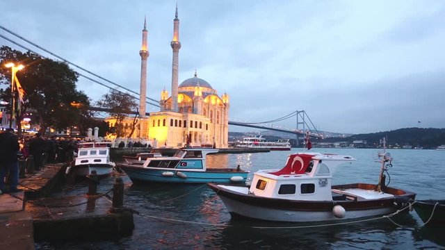 Ortakoy mosque and Bosphorus bridge in Istanbul at dusk, Turkey. Long exposure shot with blurred fishing boats on the little harbor. Vintage filter applied to warm up the mood of the photo.