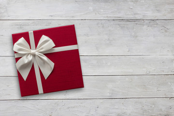 Red gift box with white ribbon over white wood, top view with copy space background