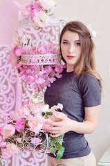 Beautiful young woman with long blonde hair, blue eyes, flowering cage, wearing t-shirt. Spring mood in pink rose tones
