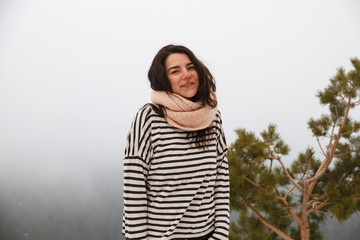 Portrait of a pretty caucasian girl on the mountain in a snowy day with foggy background. She is on a travel trip and enjoys the scenery and freedom. 