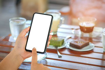 Smartphone in hand with coffee and cake on table.