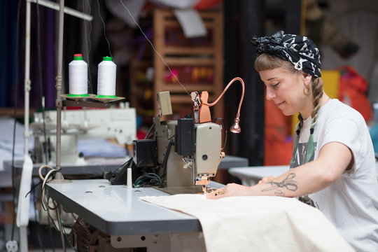 Young tattooed seamstress sewing in a factory environment