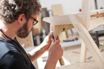 Furniture maker chiselling a chair joint in his workshop - obrazy, fototapety, plakaty