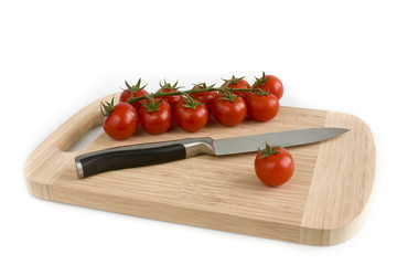 Bunch of cherry tomatoes with green leaves lying on a cutting board, isolated on white background. Still-life studio shot taken with soft-box.