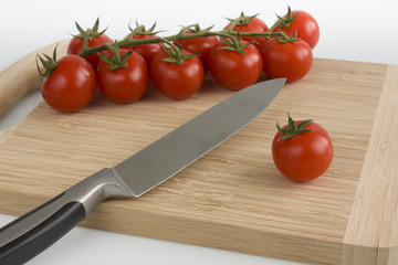 Bunch of cherry tomatoes with green leaves lying on a cutting board, isolated on white background. Still-life studio shot taken with soft-box.