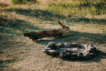 The area for a barbecue on a green grass of a garden meadow. Wooden handmade benches are painted with gray paint. The brazier is made of granite stones. The lamp will light a night party