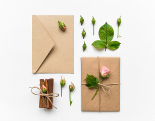Gift box and envelope in eco paper on white background. Presents decorated with roses. Holiday concept, top view, flat lay