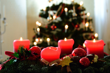 Adventskranz mit vier brennenden roten Kerzen vor Weihnachtsbaum