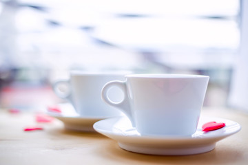 Couple cups decorated by red hearts on wooden table.
