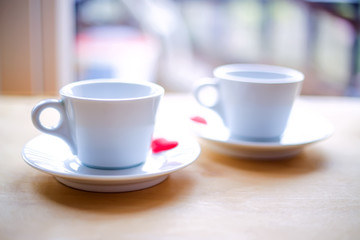 Couple cups decorated by red hearts on wooden table.