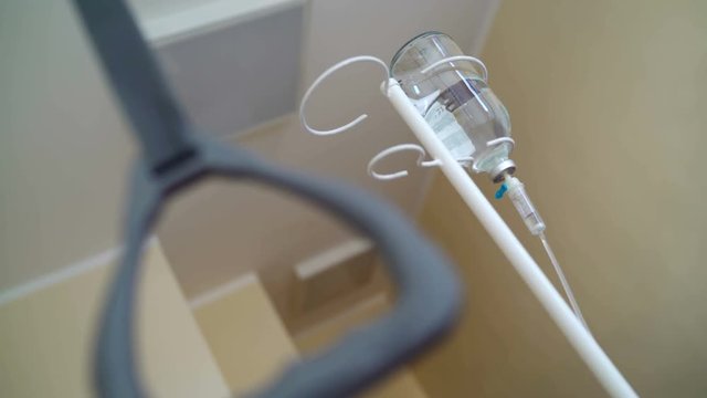 Patient POV from hospital bed. IV drip stand with infusion bottle. A person receiving saline solution via intravenous therapy.