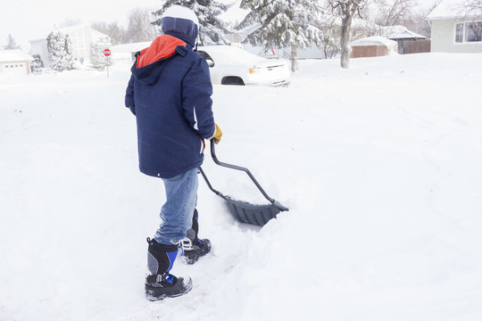 horizontal image of a man wearing jacket and boots out shovelling the deep snow off his driveway after a big snow storm.