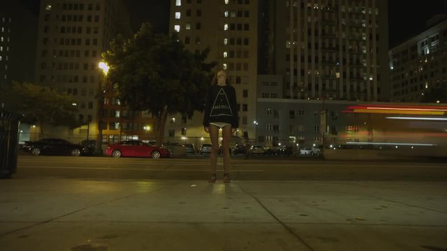 Girl staying on the downtown street and looking on a tall building. Girl stopped and looking up. Time Lapse night city on background
