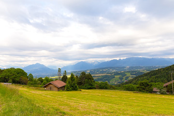Panoramic view of Swiss Alps near Geneva, Switzerland. Farmhouses and hilly countryside on a cloudy day in summer.