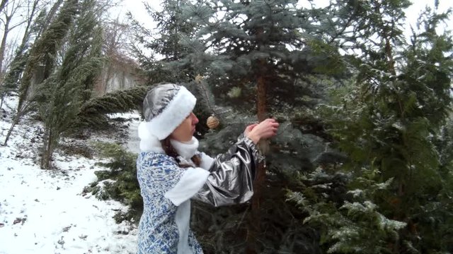 Snow Maiden in forest hanging toys on a firm tree smiling Ukraine.