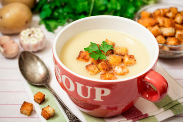 Homemade potato cream soup with croutons and parsley in red bowl on table