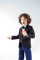 Cute curly boy stands and sings into the microphone in a business suit. Full length. Gray background.