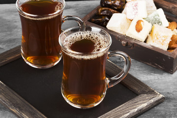 Black tea, oriental sweets, dates and nuts on a dark background