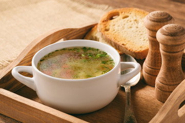 Chicken soup in white bowl on wooden tray.