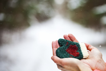 Close up: female hands hold a Green mitten with heart ornament. Love concept.