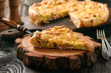 Homemade quiche with leek, ham and cheese on wooden background.