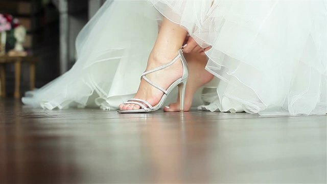 Woman puts on shoes hands close up shallow depth of field. Bride fastens zipper on luxurious high heeled sandals sitting in gorgeous white gown getting ready prepared for dancing at wedding ceremony 