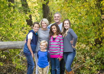 A smiling, happy, large beautiful family portrait. Standing together and hugging each other outdoors with a forest in the background