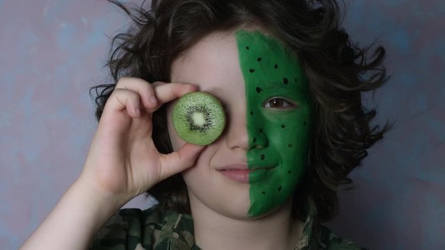 4k Shot of a Cute Child with Coloured Face posing with Kiwi