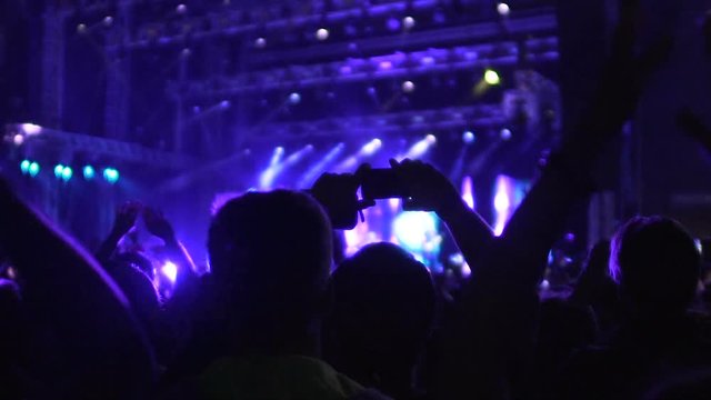 Silhouettes of many people applauding and filming video on phone at concert
