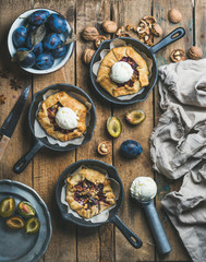 Plum and walnut crostata pie with ice-cream scoops in individual cast iron pans over rustic wooden table, top view. Slow food concept