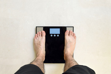 Man's view of him standing on a black bathroom scale