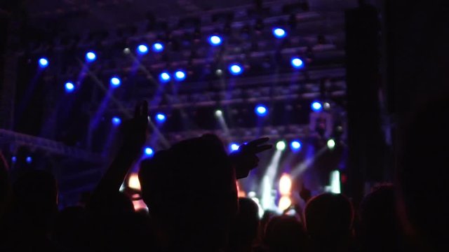 Silhouettes of happy people enjoying music at concert, waving hands in air