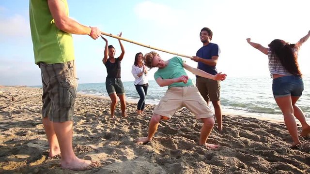 Friends dancing limbo at beach. Multiracial group of people enjoying time together, playing and dancing at seaside