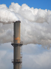 Vertical image of an old smokestack with smoke and steam billowing around. Copy space.