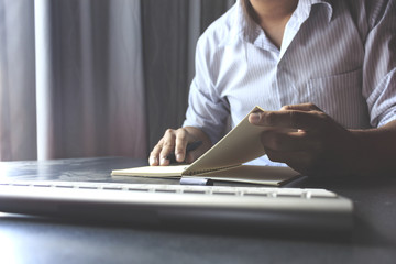 businessman reading a book and writing notes on wooden table with film colors tone, soft-focus in the background. over light