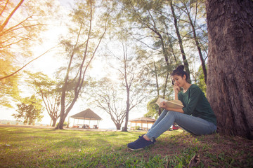 Beautiful young asian woman sitting and reading book in a park