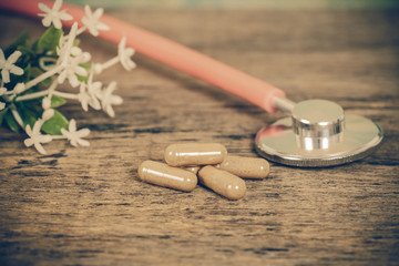 herb capsules and stethoscope on wood table