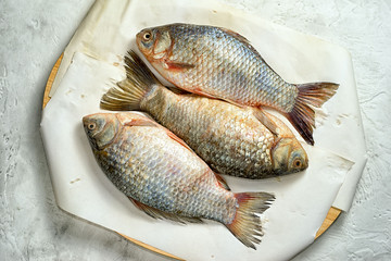 Three fresh carp on a cutting board with paper, top view