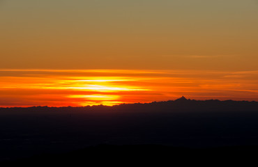 Fiery sunset from mountain pick with thin glazes in the sky evening. Fall season. Orobie alps. Rena pick. Bergamo Italy. In the distance the Monviso.