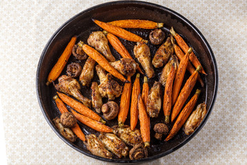 Roasted chicken wings with carrot and mushrooms on a tray
