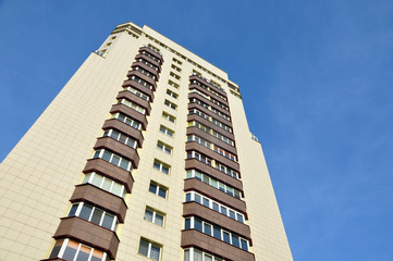 Looking up at the modern multistory residential building on a background of blue sky.