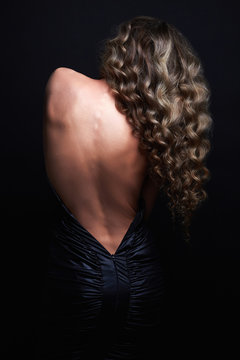 beautiful back of young woman in a black sexy dress.luxury beauty brunette Girl curly healthy hair