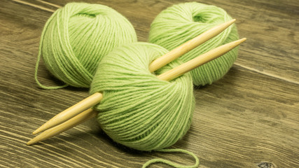 Wolle im Knäuel in Hellgrün, mit Stricknadeln auf einem Holzuntergrund